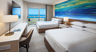 Image of two beds and work area leading to a balcony  in an Oceanfront Room.