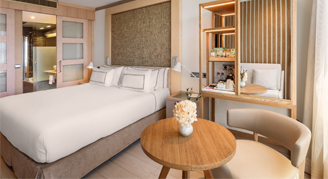 Image of bedding, small table and chair in a Deluxe Room.