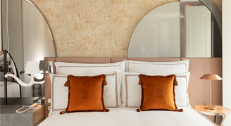 Image shows  a plush king bed with burnt-orange accent pillows.