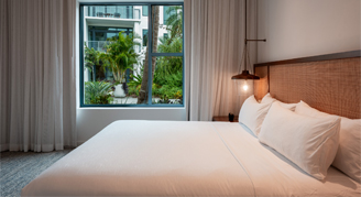 The image shows a modern bed with pillows and a view outside of the flat.