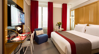 Hotel room with a queen bed, lamps and a writing desk.