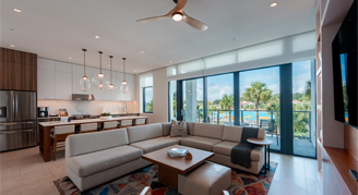 The image shows a family area with a kitchen and dining area in the background and a view outside.