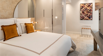 Image shows  a plush king bed with burnt-orange accent pillows.