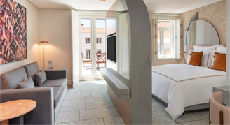 Image shows  a plush king bed with burnt-orange accent pillows separating the living room area with a divider wall.