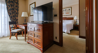 Ambassador Suite featuing classic-style study area with a wooden desk and a television positioned on a matching wooden chest. 