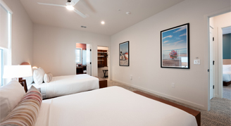 The image shows a bedroom with white walls, a white ceiling fan, and framed artwork hanging on the wall.