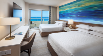 Image of two beds and work area leading to a balcony  in an Oceanfront Room.