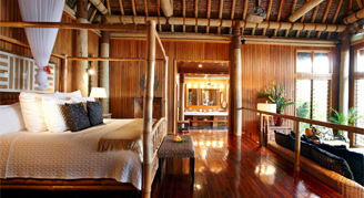 A view of the inside of the Villa at Namale Resort & Spa, featuring a large bed, seating area and a bathroom in the background.