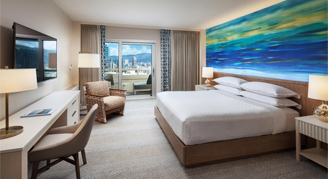 Image of a bed and work area leading to a balcony in a Partial-Ocean-View Room.