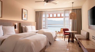 Interior view of the Premium-Ocean-View Junior Suite with two double beds overlooking ocean.