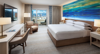 Image of a bed and work area leading to a balcony in a Partial-Ocean-View Room.