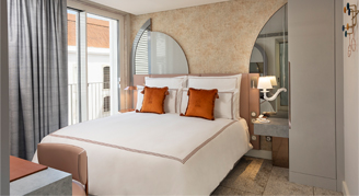 Image shows  a plush king bed with burnt-orange accent pillows.
