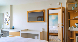 Image shows a wall-mounted television, and an open connecting doorway leading into an adjacent room.