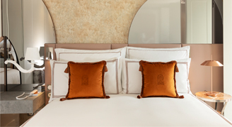 Image shows  a plush king bed with burnt-orange accent pillows.