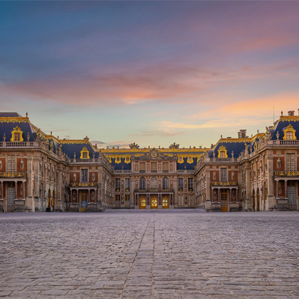 The grand entrance of the Palace of Versailles at sunset, with its ornate façade and symmetrical wings bathed in warm light.