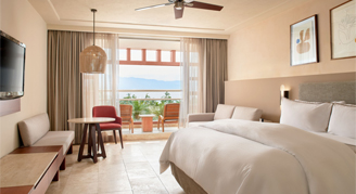 Interior view of the Partial-Ocean-View Junior Suite with a single king bed overlooking the trees and ocean.