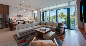 The image shows a family area with a kitchen and dining area in the background and a view outside.