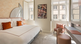 Image shows  a plush king bed with burnt-orange accent pillows and desk area.