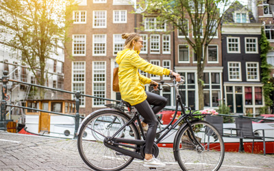 Young woman in yellow raincoat with bag and flowers riding a bicycle in Amsterdam city.